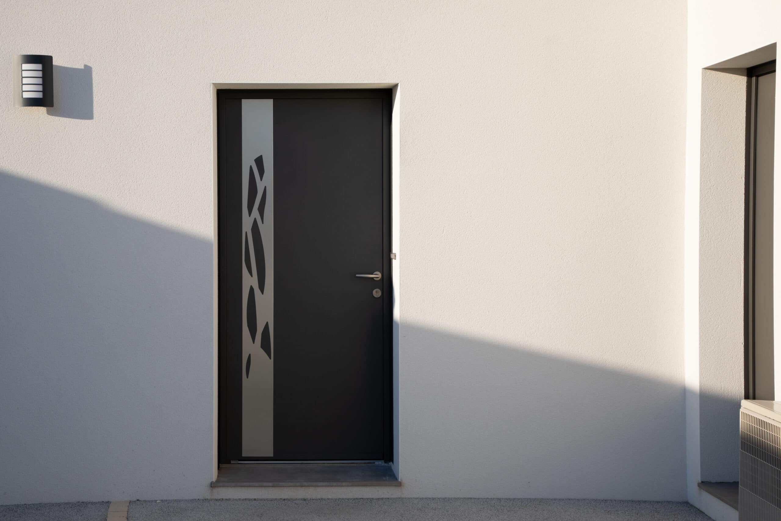 Façade moderne blanche avec porte d'entrée anthracite et motif abstrait. Applique murale design, fortes ombres solaires, unité de climatisation.