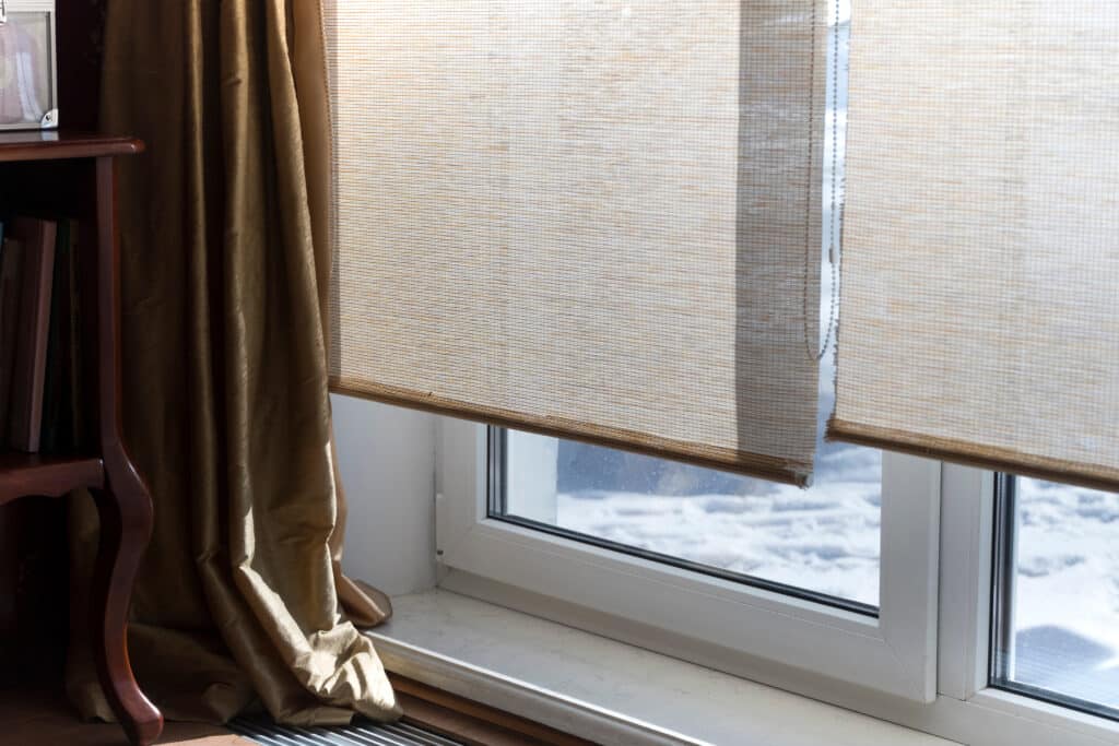 Stores enrouleurs beige: Fenêtre, rideaux dorés et hiver lumineux Fenêtre avec stores enrouleurs beiges, rideaux dorés. Paysage enneigé. Lumière du soleil. Livres (dont « ЩЕЛКУНЧИК ») sur étagère bois.